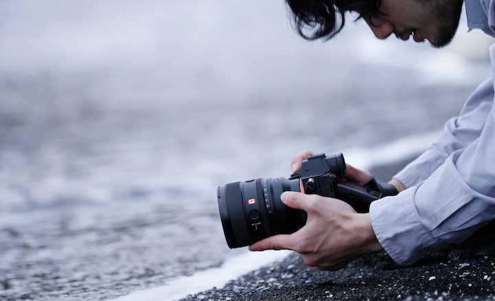 Se ve a un fotógrafo arrodillado al borde del agua, capturando fotos en un ángulo que sugiere que podría estar sumergido en el mar.